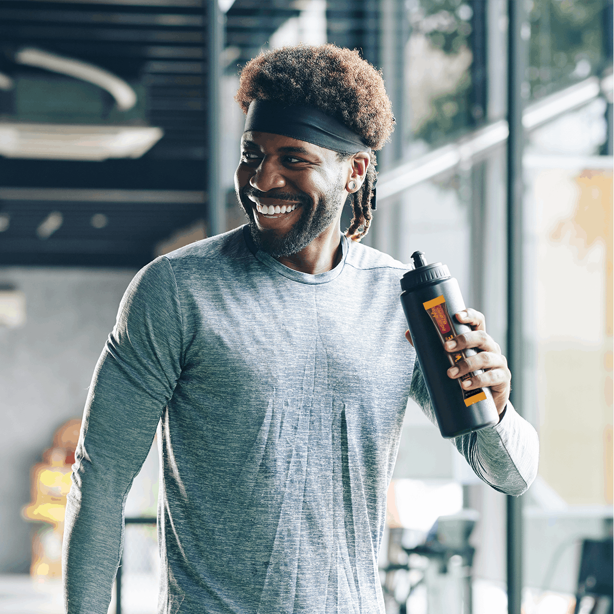 Man in athletic wear holding a water bottle and gym bag in a gym setting